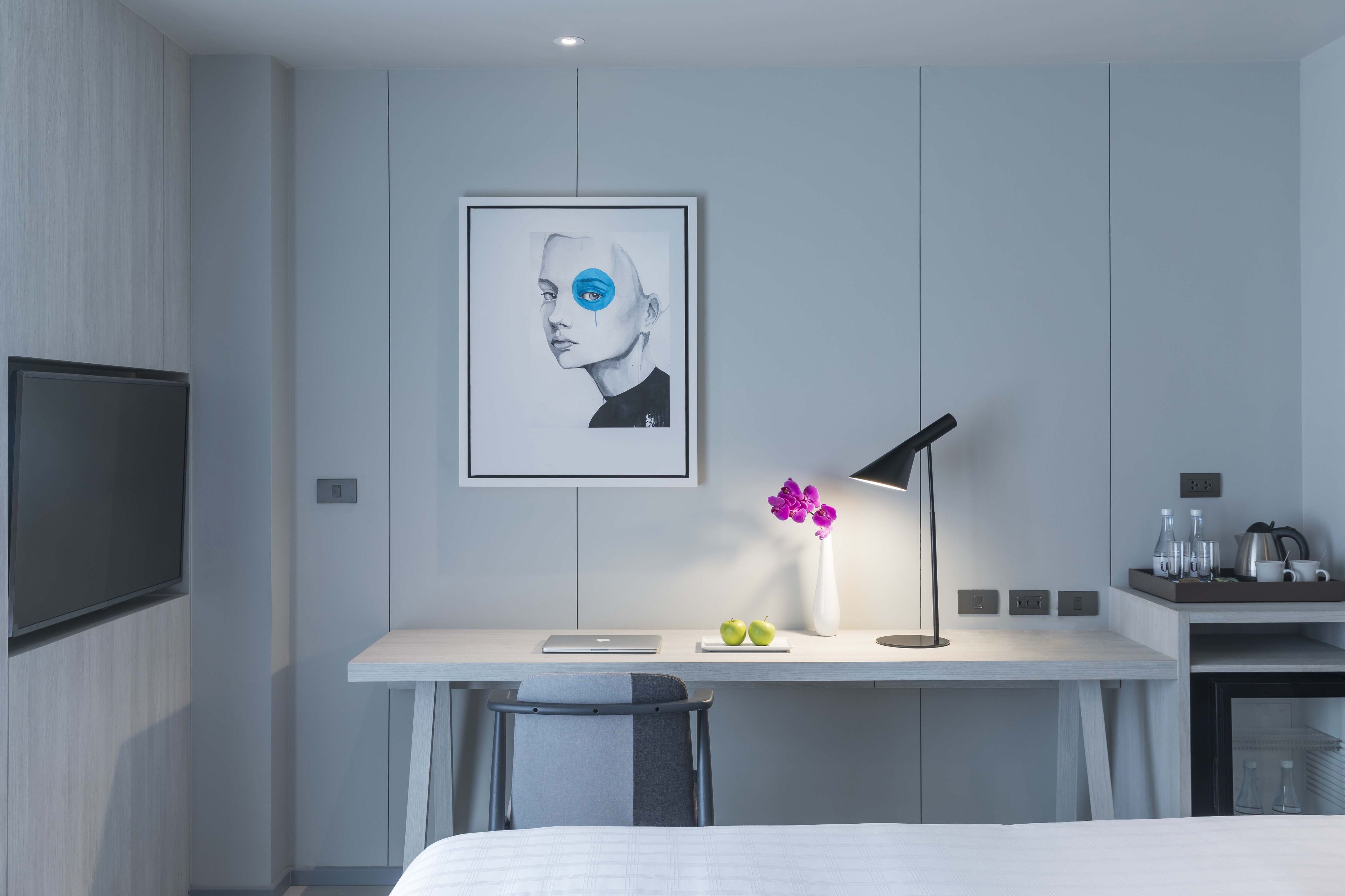 Habitació d'hotel moderna amb un disseny minimalista, que destaca un escriptori blanc, un ordinador portàtil, un ram de flors i una obra d'art emmarcada a la paret.