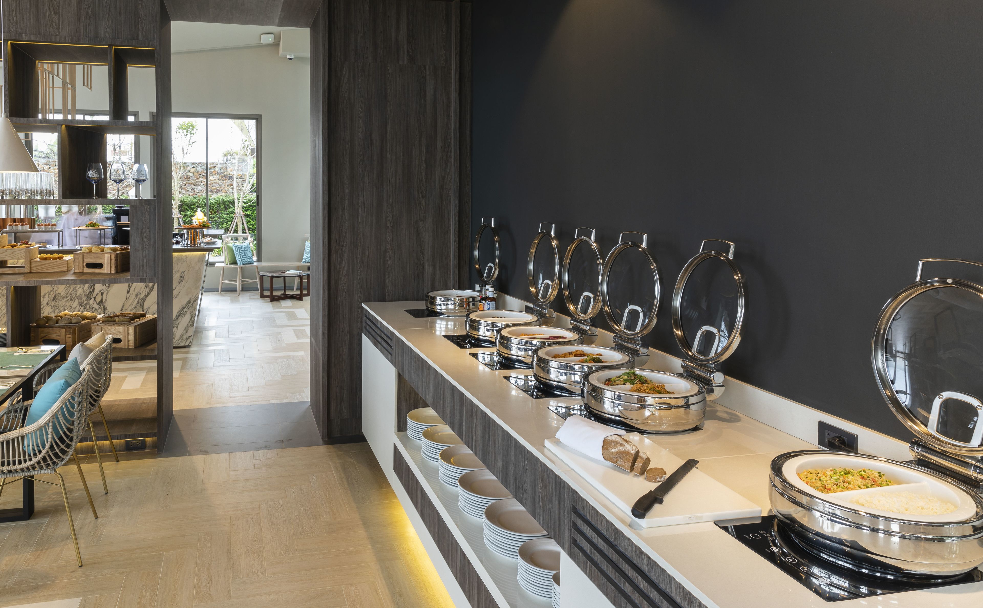 A buffet area with multiple serving stations, a seating area with chairs, and a view of the outdoors.