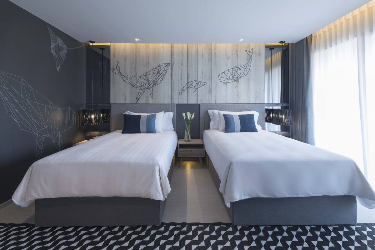 Una habitación de hotel moderna con dos camas, un espejo grande y decoración mural geométrica.