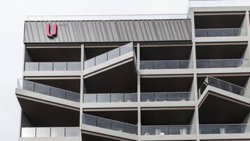 Een meerlaags gebouw met een modern architectonisch ontwerp, voorzien van balkons met glazen hekwerk en een opvallend logo bovenaan.
