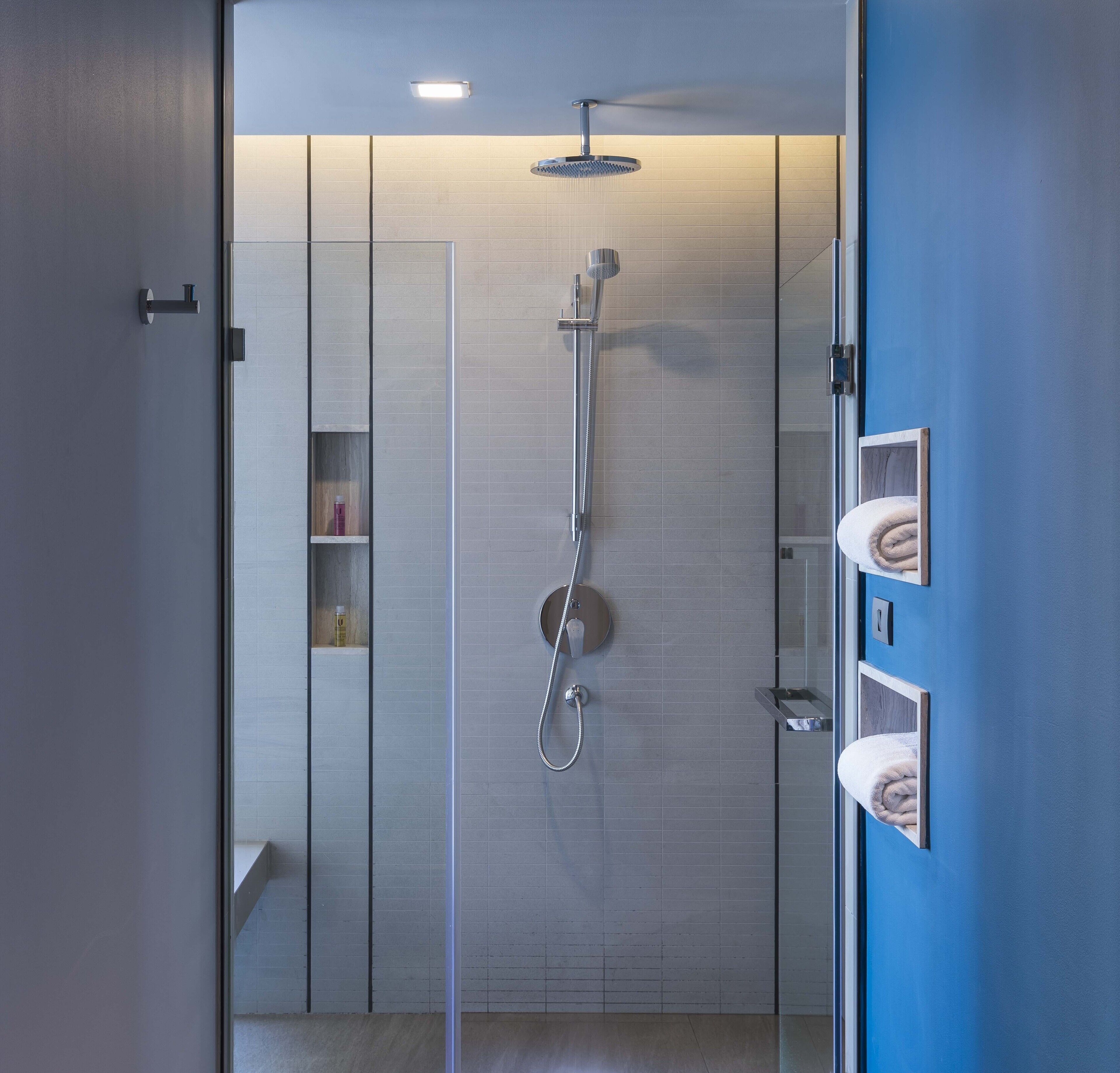 Una ducha moderna con puerta de vidrio, cabezal de ducha de mano y panel de control en la pared.