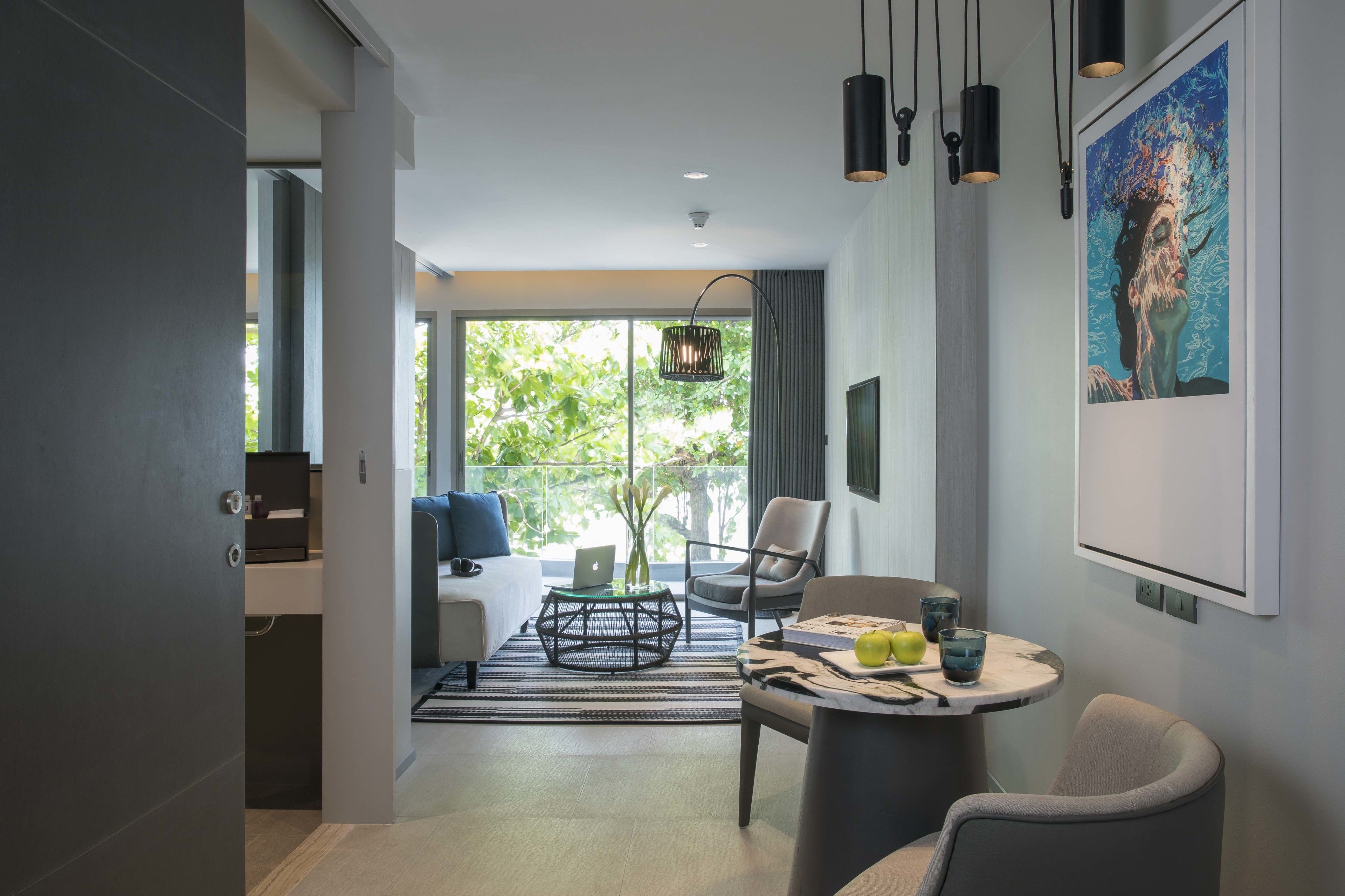 A modern hotel room with a large window, a sofa, a dining table, and a chair.