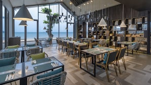A restaurant with tables and chairs, large windows, and hanging lights.