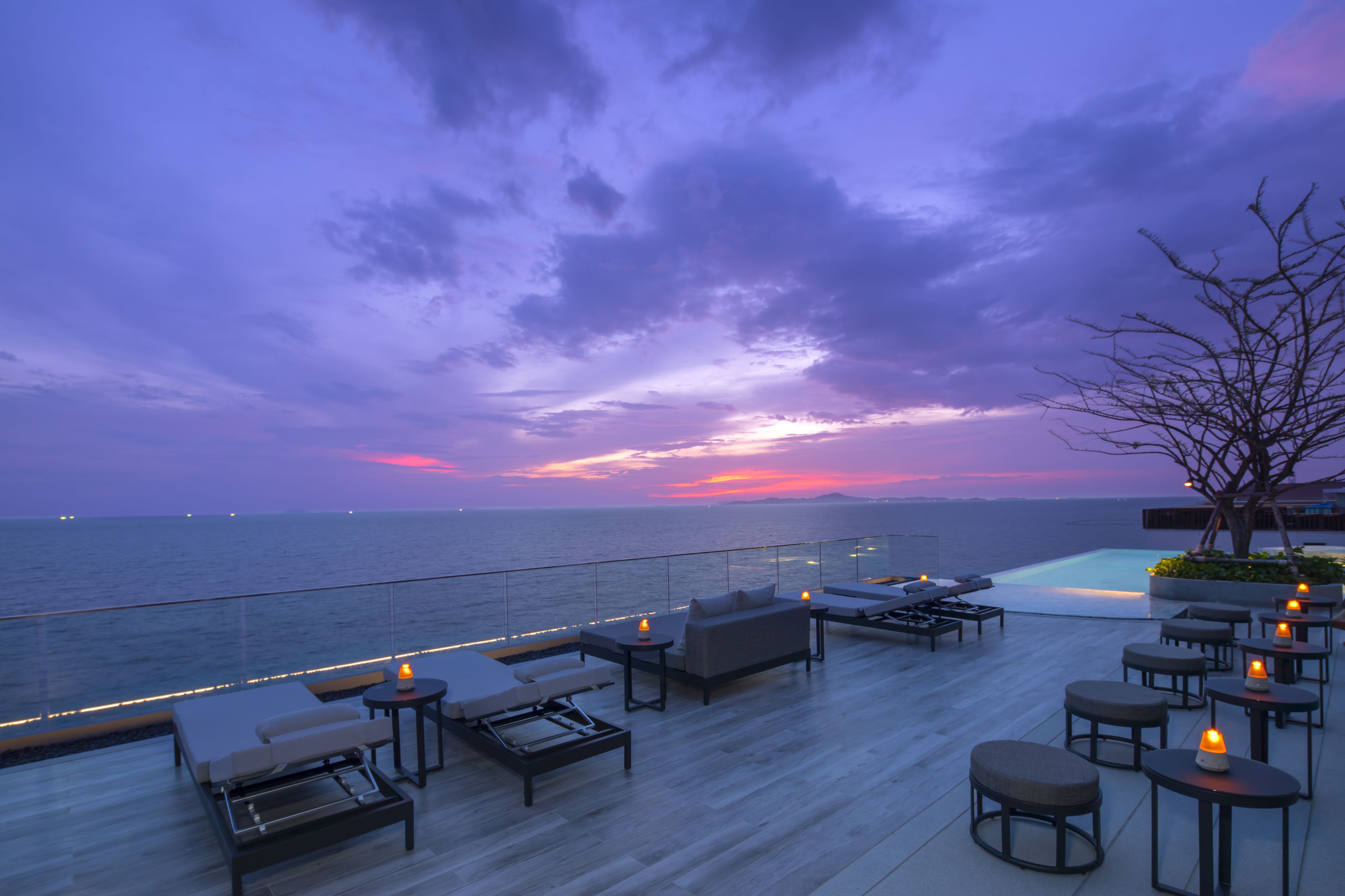 A rooftop terrace with outdoor seating and a view of the ocean at sunset.