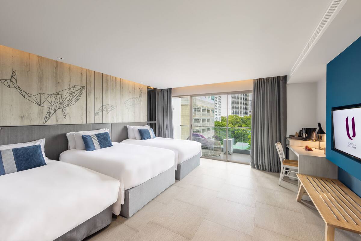 Una habitación de hotel moderna con dos camas, un escritorio, una silla y un balcón con vistas a la ciudad.