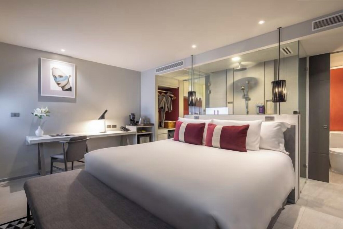 Habitación de hotel moderna con una cama grande, un escritorio, una silla, un espejo y zona de ducha.