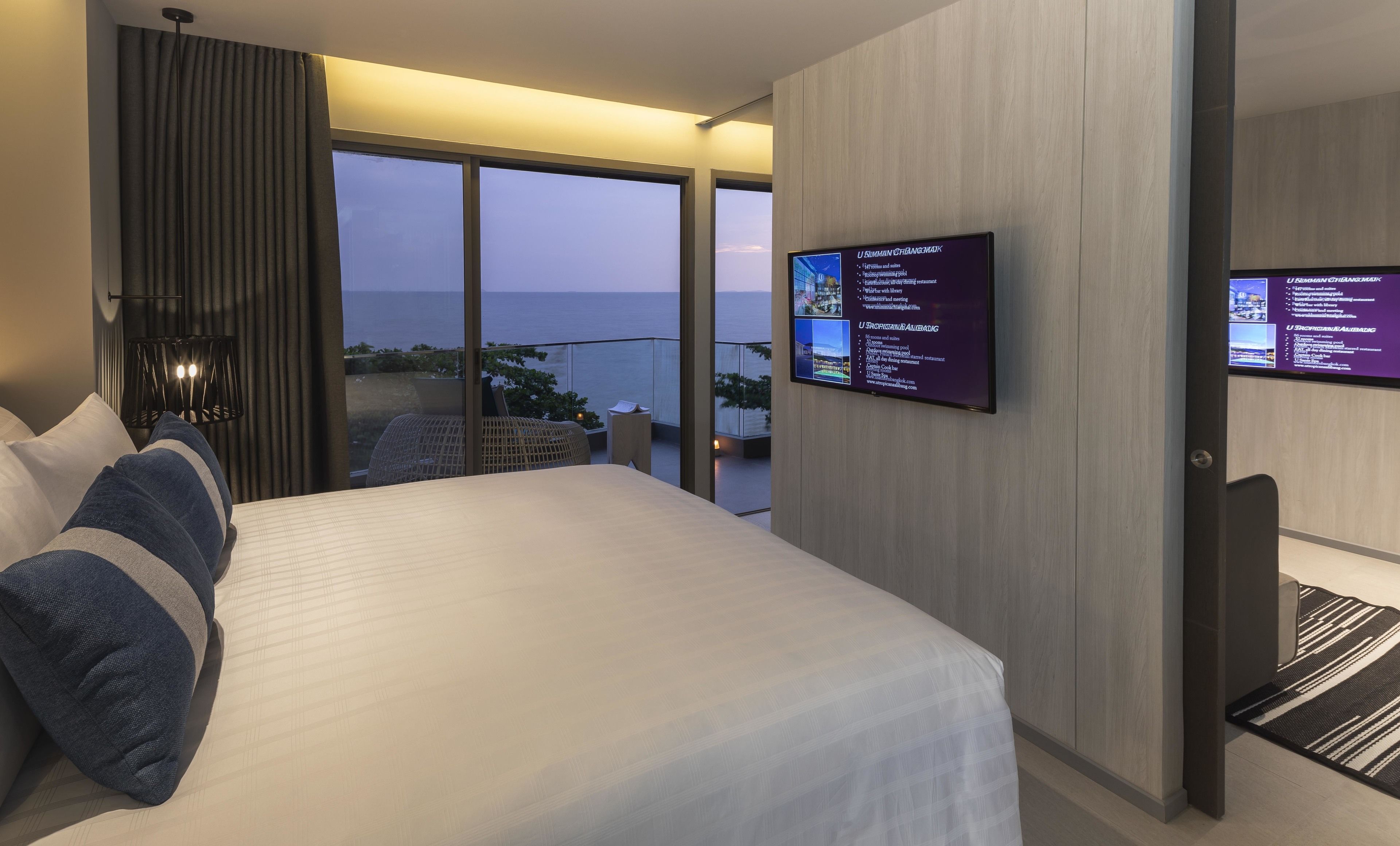 Une chambre d’hôtel moderne dotée d’un grand lit, d’un téléviseur fixé au mur et d’un balcon offrant une vue sur la mer.