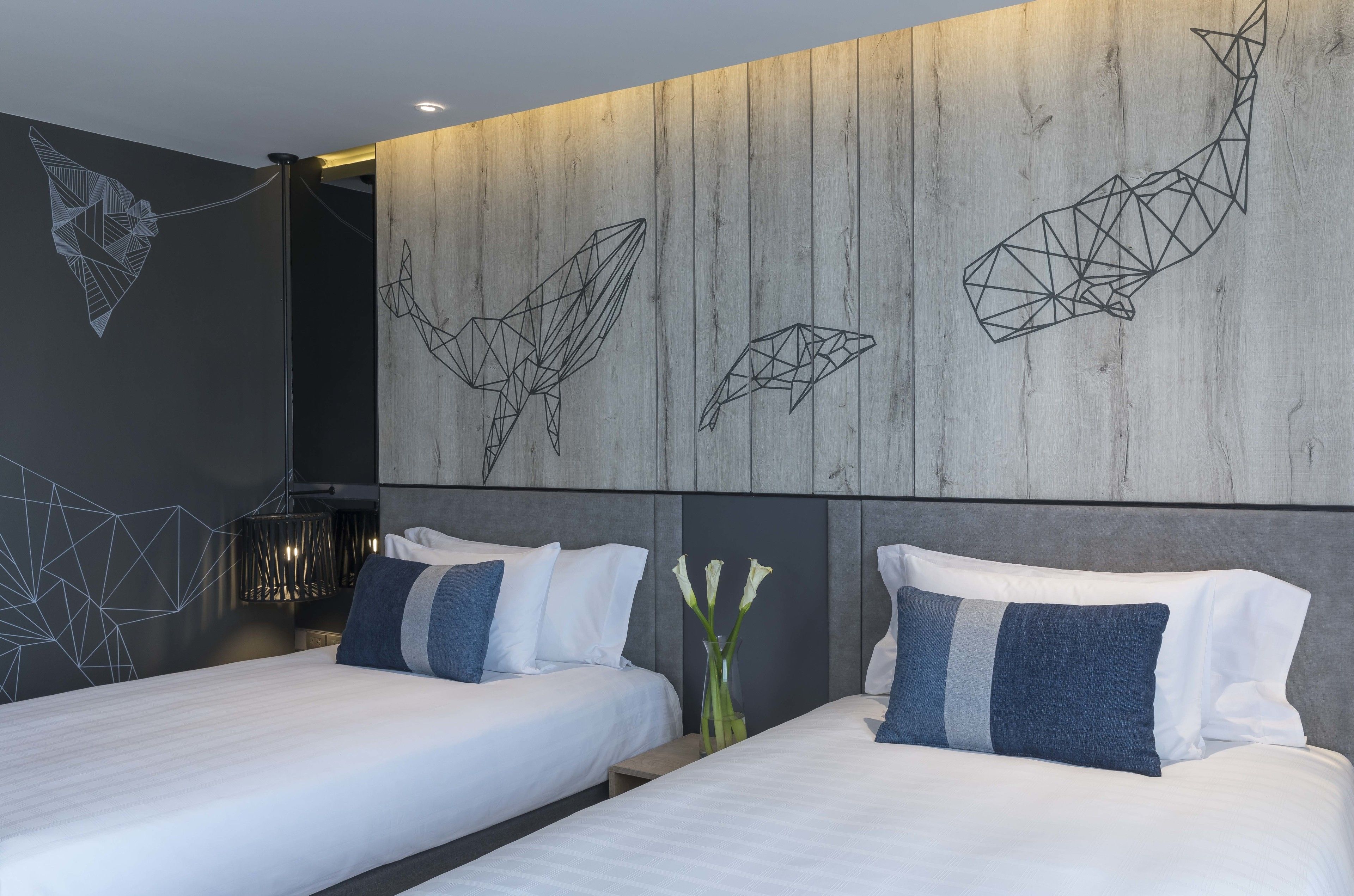 A modern hotel room with two beds, geometric wall art, and a wooden accent wall.