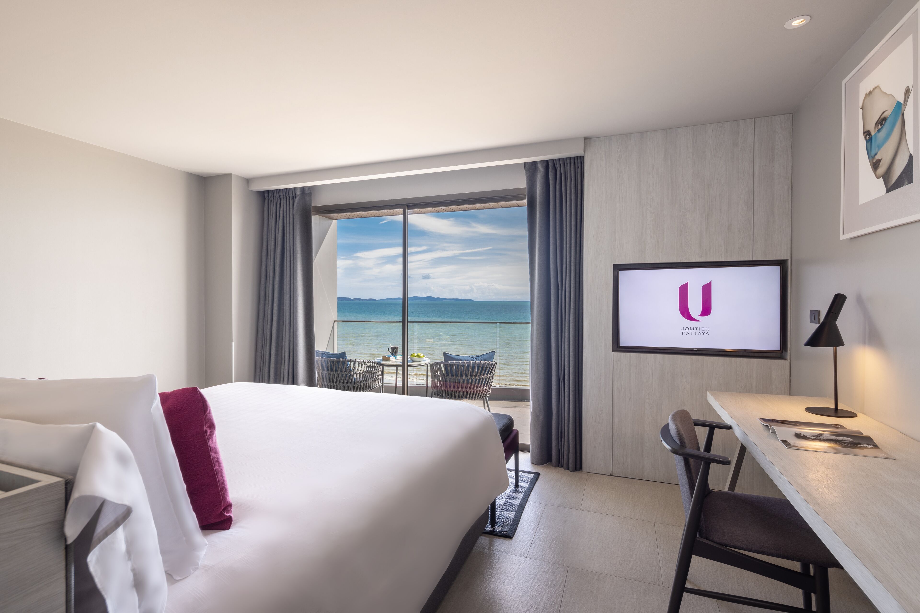 Ett hotellrum med en stor säng, ett skrivbord, en stol och en tv som visar hotellets logotyp.
