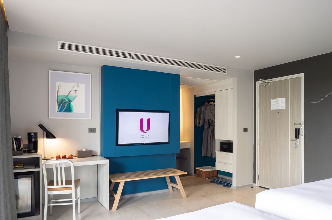 Una habitación de hotel moderna con escritorio, una banca, cama y armario.