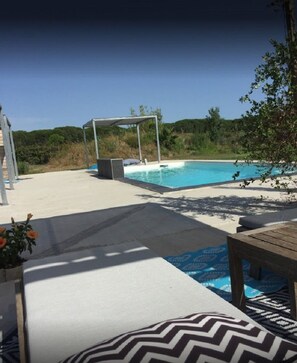 Een zwembadgedeelte met een pergola, ligbedden en een houten tafel.