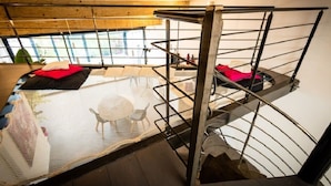 A modern interior with a metal staircase, a glass table with a decorative item, and a view through large windows. - Suites d'hôtes Prestige Mas de l'étoile (Saint-Laurent-d'Aigouze)