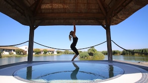 A person performing an aerial yoga pose on a circular pool under a thatched roof structure. - Suites d'hôtes Prestige Mas de l'étoile (Saint-Laurent-d'Aigouze)