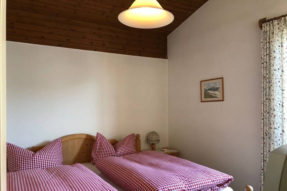 Une chambre avec deux lits, des têtes de lit en bois, une table de chevet, une lampe et un tableau encadré au mur.