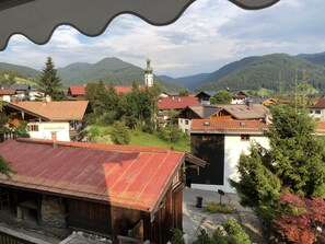 A traditional wooden building with a red roof, surrounded by greenery and a mountainous backdrop. - Haus Dippold (Reit im Winkl)