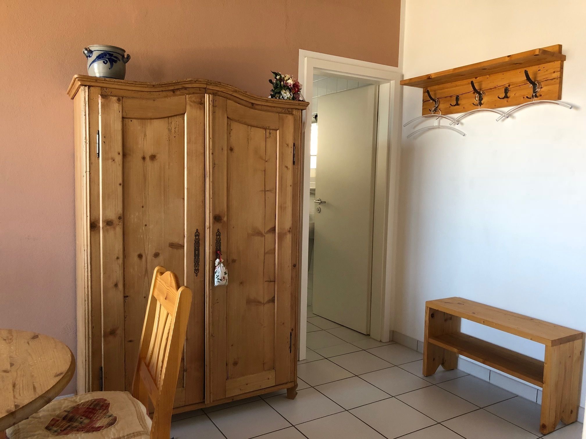 A wooden wardrobe with a small table and bench in a room with tiled flooring.