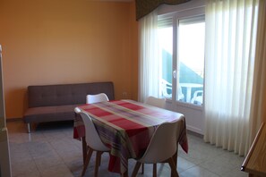 A dining area with a table and chairs, a sofa, and a window with curtains. - Apartamentos Los Gemelos (Foz)