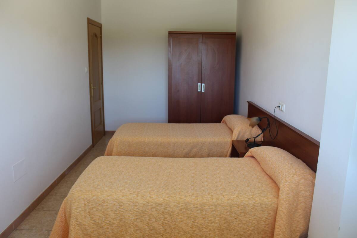 A room with two beds, a wardrobe, and a power outlet on the wall.