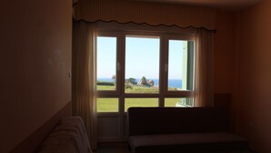 Quarto com sofá e janela com vista para o mar e uma casa ao longe.
