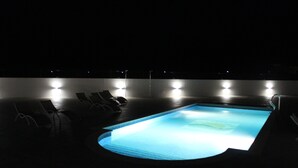 Uma piscina com algumas espreguiçadeiras e luzes na borda.