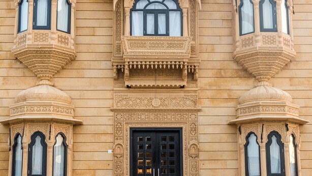 A building with intricate architectural details, including ornate balconies and a central entrance with a black door. - The Legend Haveli (Jaisalmer)