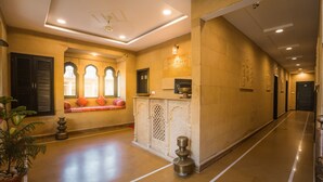 A hotel lobby with a reception desk, seating area, and a decorative wall with traditional motifs. - The Legend Haveli (Jaisalmer)