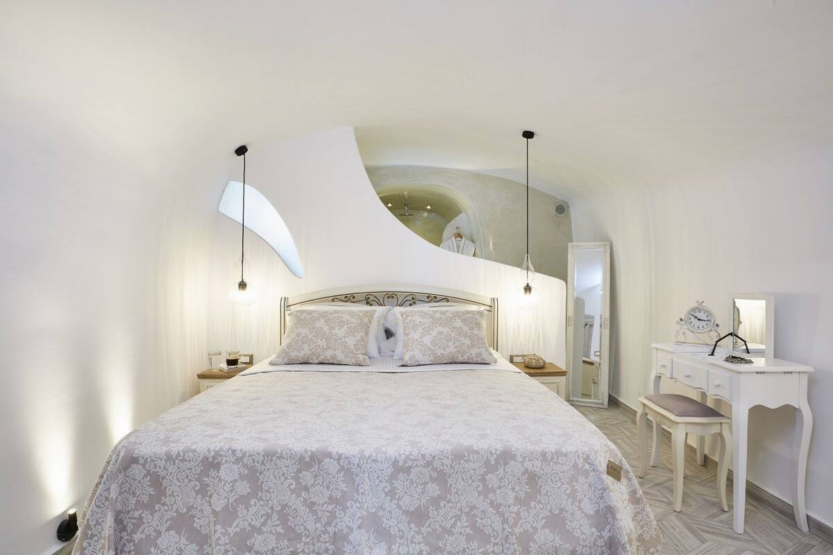 A bedroom with a large bed, a vanity with a mirror, and a wall-mounted clock.
