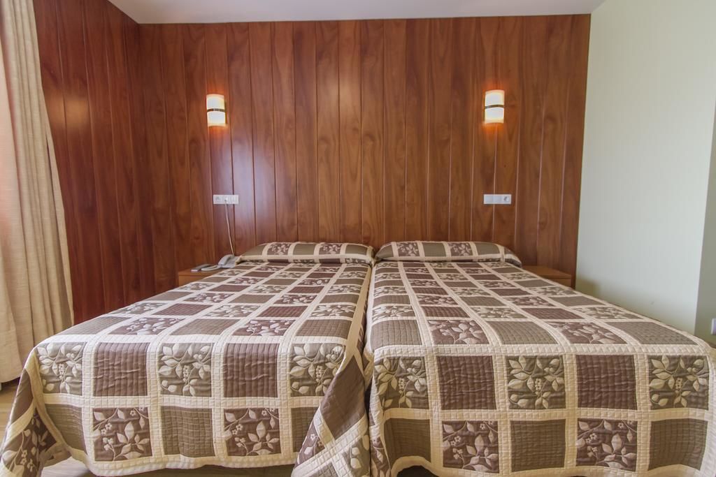 A room with two beds, wooden panel walls, and two wall-mounted lights.
