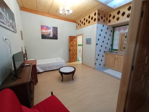 A room with a bed, a small table, a TV, and a wooden ceiling.