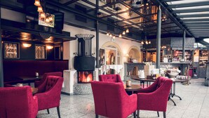 A restaurant with red upholstered chairs, a fireplace, and a reception area. - Schlosshotel Neufahrn (Neufahrn in Niederbayern)