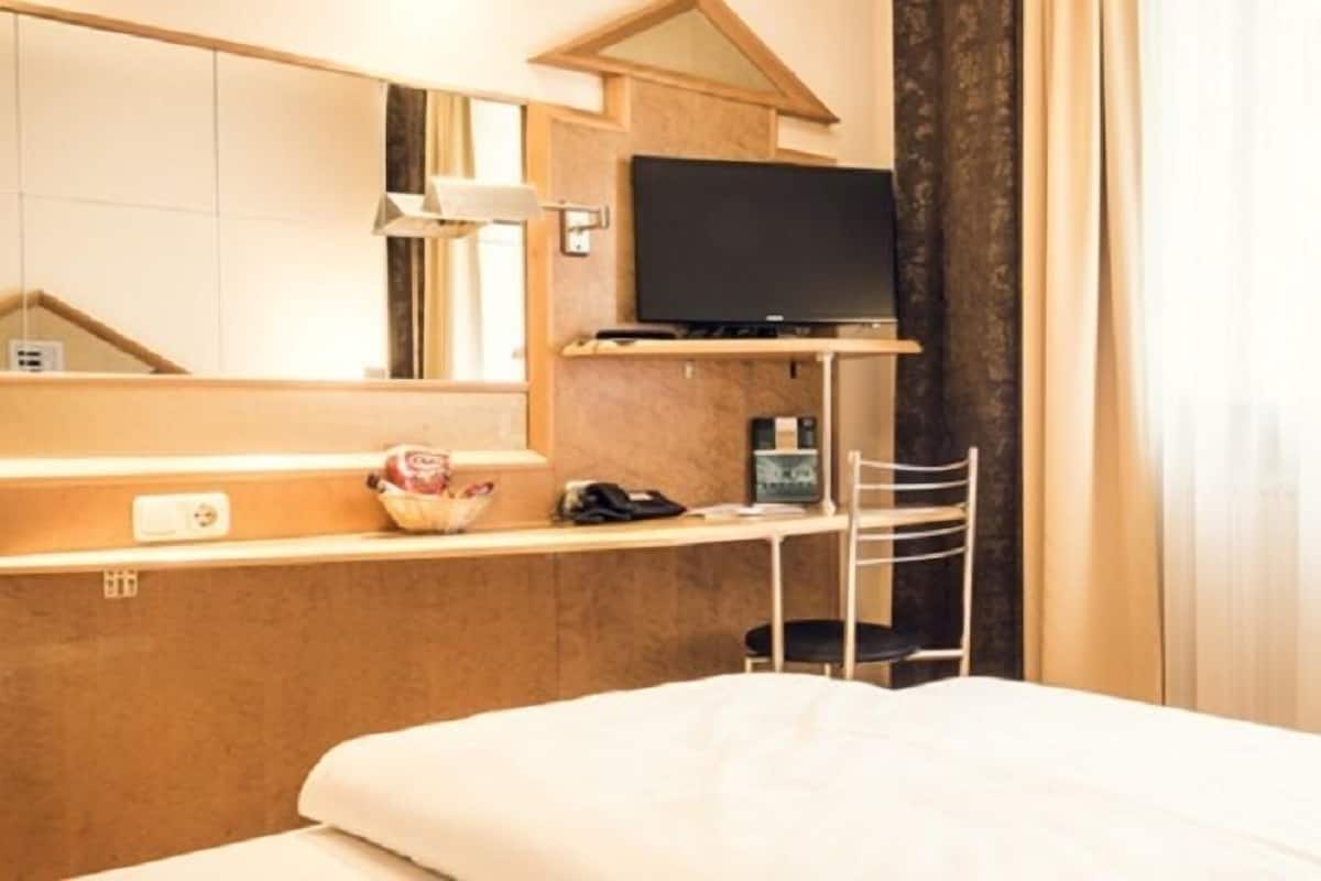 A hotel room with a bed, a desk with a television, a telephone, and a small table with a basket.