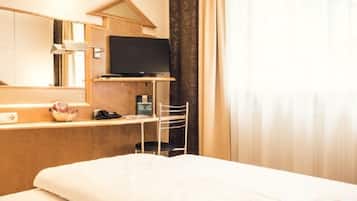 A hotel room with a bed, a desk with a television, a telephone, and a small table with a basket.