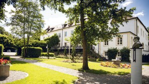 A well-maintained garden with a pathway leading to a building with multiple windows and a statue. - Schlosshotel Neufahrn (Neufahrn in Niederbayern)