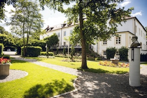 Um jardim bem cuidado com um caminho que leva a um edifício com várias janelas e uma estátua.