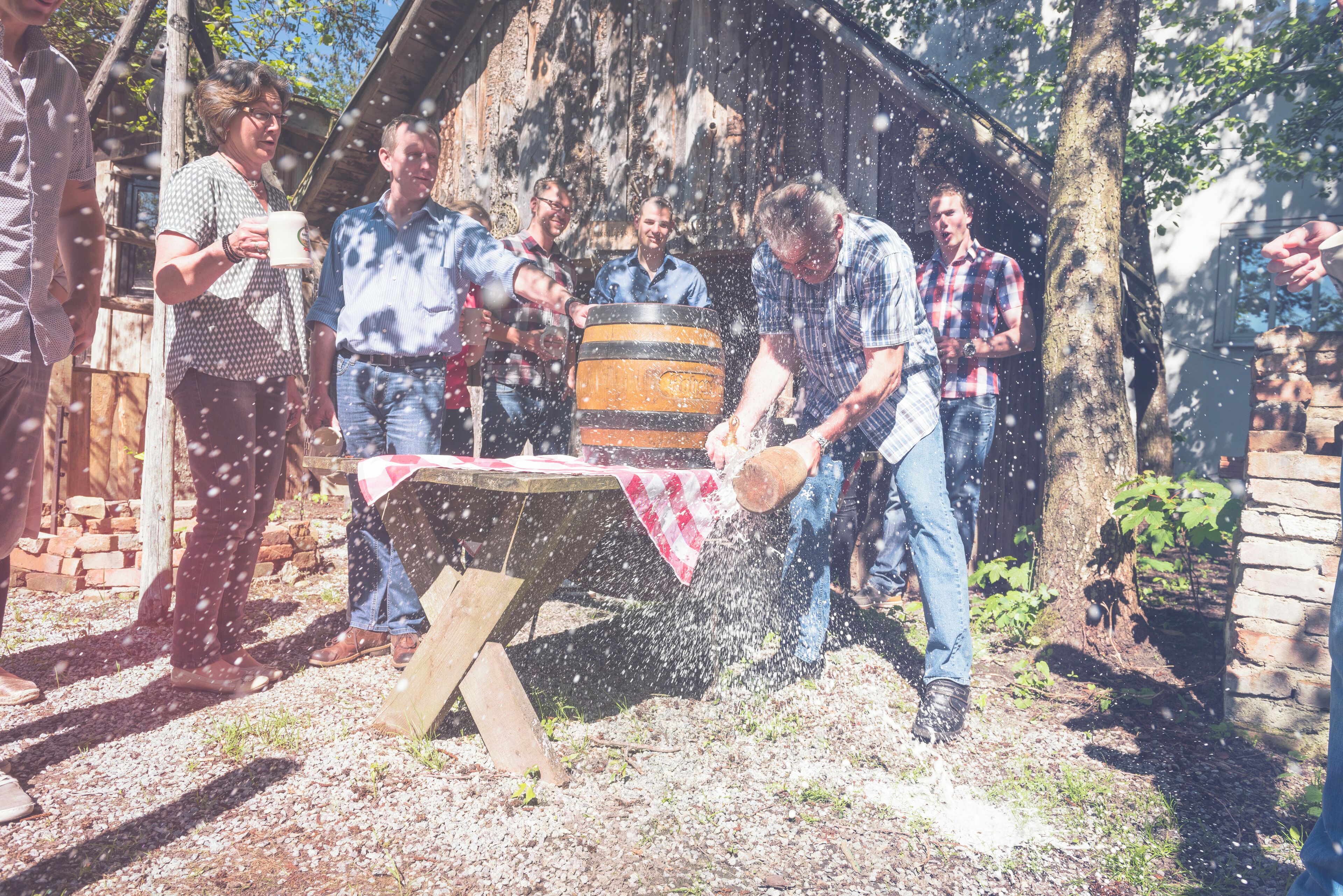 A group of people outdoors, some standing and some sitting, around a table with a flag on it.