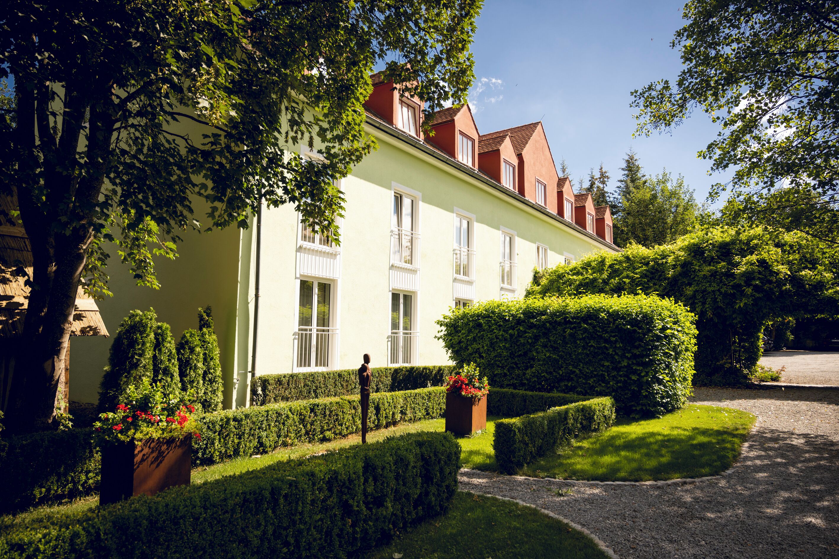 A building with a light facade, multiple windows, and a well-maintained garden with hedges and flower boxes.