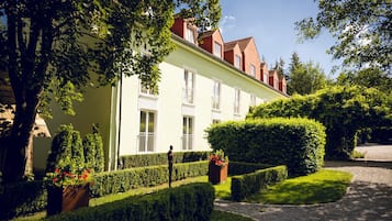 A building with a light facade, multiple windows, and a well-maintained garden with hedges and flower boxes.