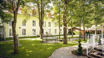 A courtyard with a circular gravel area, surrounded by trees and a building with multiple windows.