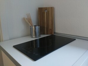 A kitchen with a black induction cooktop, a stainless steel utensil holder, and a wooden cutting board.