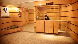 A reception area with wooden paneling, a reception desk, a fire extinguisher, and a vase with flowers. - Hostal Terra Chá (Villalba)