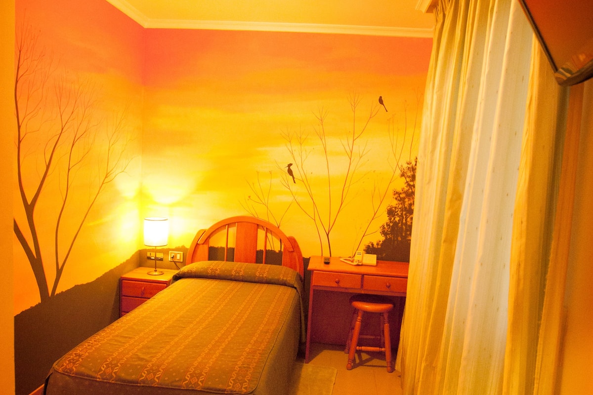 A bedroom with a bed, a desk, a chair, and a nightstand.