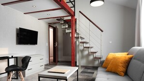 A modern living room with a grey sofa, a black chair, a white table, and a staircase with wooden steps and metal railings. - KRISTINA Willa & Spa (Szklarska Poreba)
