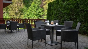 An outdoor patio with wicker chairs and tables, a wooden deck, and a hedge in the background. - KRISTINA Willa & Spa (Szklarska Poreba)