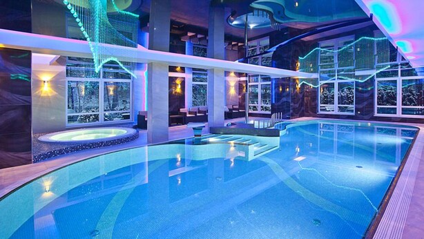 A modern indoor swimming pool with a glass ceiling, multiple hot tubs, and a view of snow-covered trees. - KRISTINA Willa & Spa (Szklarska Poreba)
