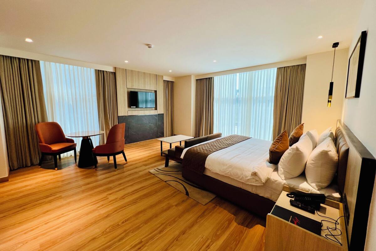 A hotel room with a bed, two armchairs, a small table, a TV, and a desk.