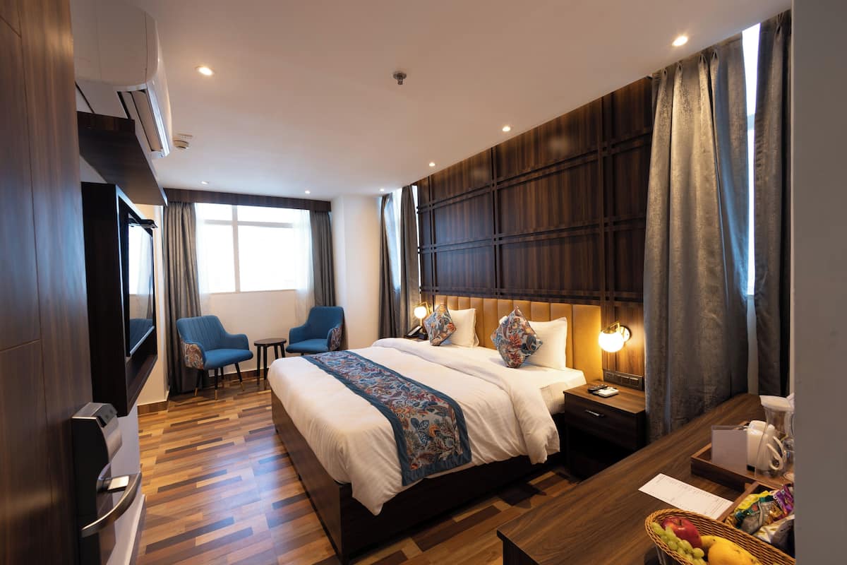 A modern hotel room with a large bed, a desk, a chair, and a TV.