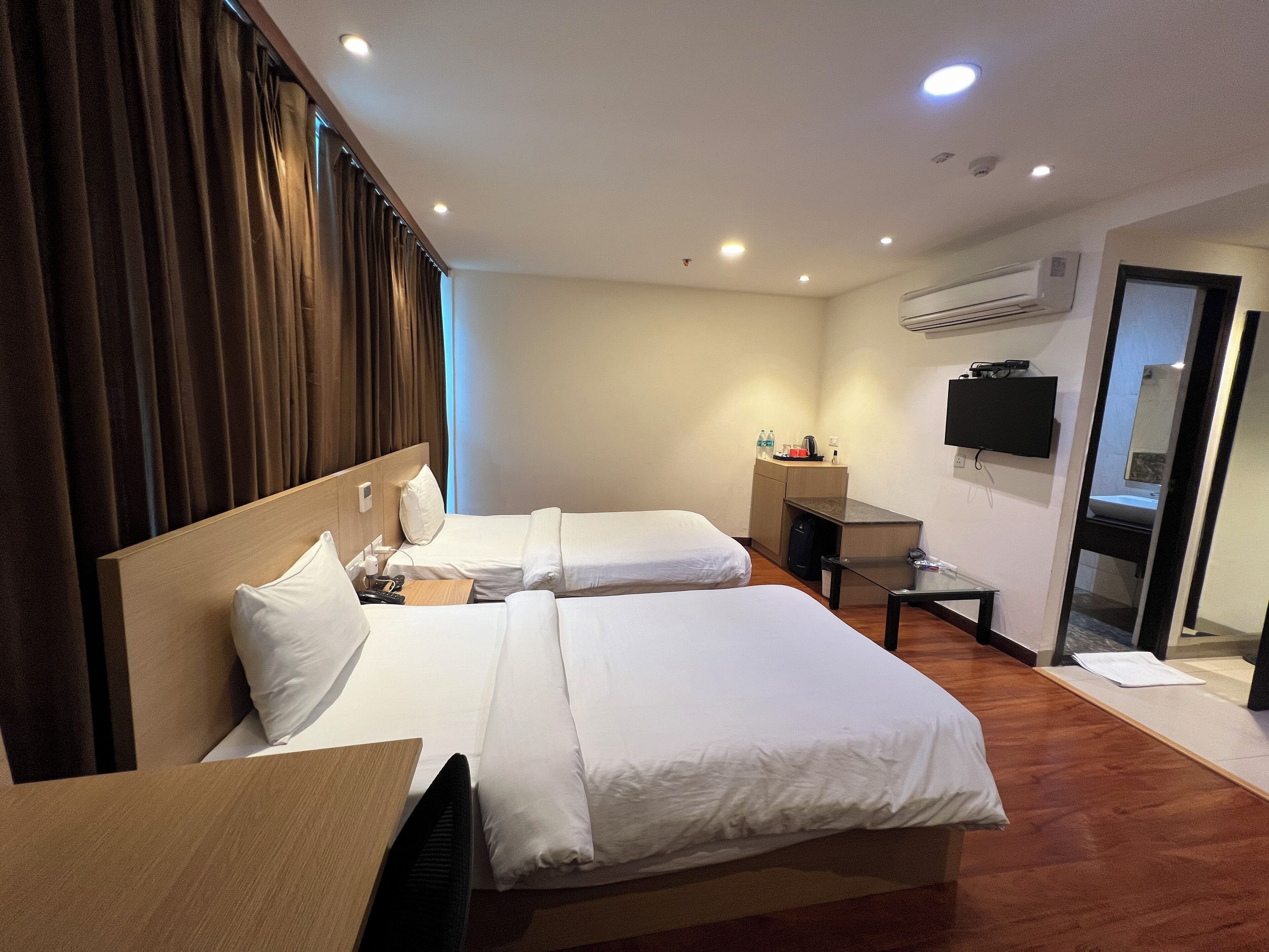 A hotel room with two beds, a desk, a chair, an air conditioning unit, a TV, and a mirror.