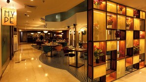 A modern hotel lobby with a polished marble floor, a seating area with tables and chairs, and a decorative wall with shelves containing flowers. - Hyphen Business Hotel (Noida)
