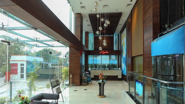 A spacious lobby with a glass wall, a reception desk, and a seating area with a vase of flowers. - Hyphen Business Hotel (Noida)