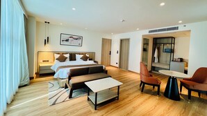 A modern hotel room with a large bed, a sofa, a small table, and a seating area with chairs. - Hyphen Business Hotel (Noida)